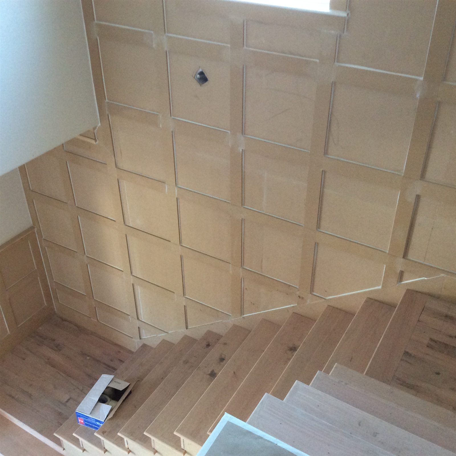 View looking down a staircase with custom geometric wall paneling and unfinished wood stair treads